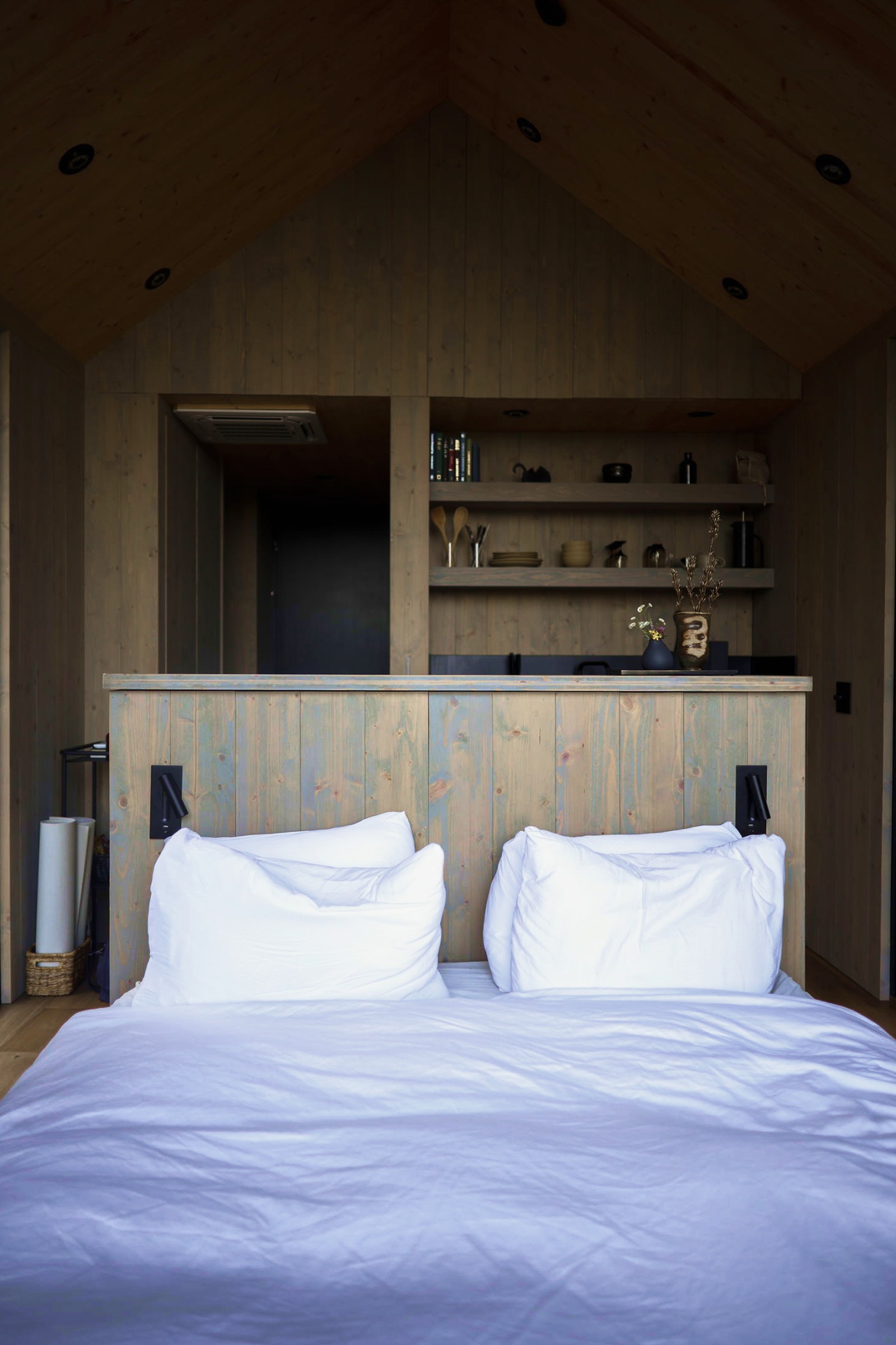 Bed under the pitched ceiling, kitchen shelves beyond