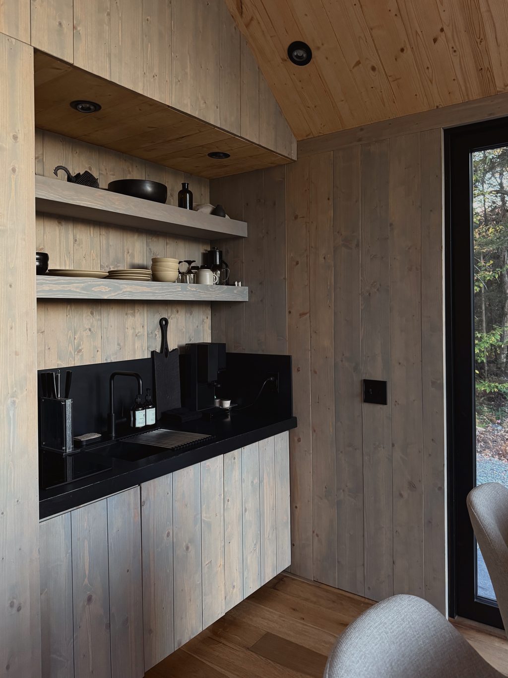 Bed beneath a pitched timber ceiling, forest through the window