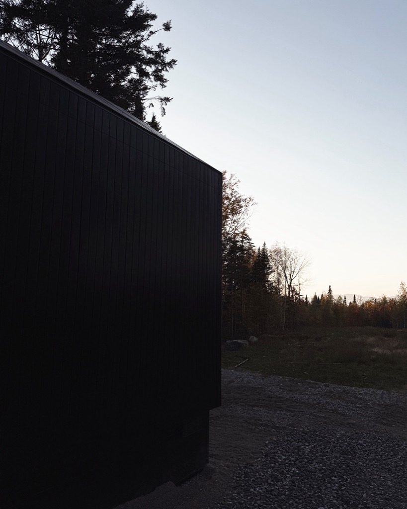 Black timber cabin at the edge of the clearing at dusk