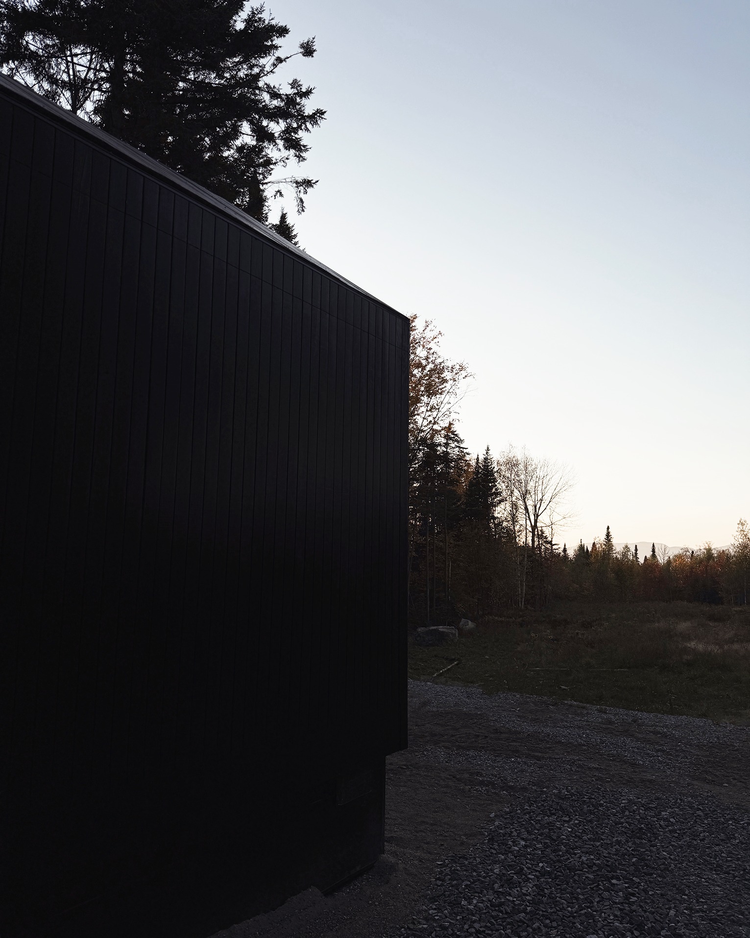 Black timber cabin at the edge of the clearing at dusk