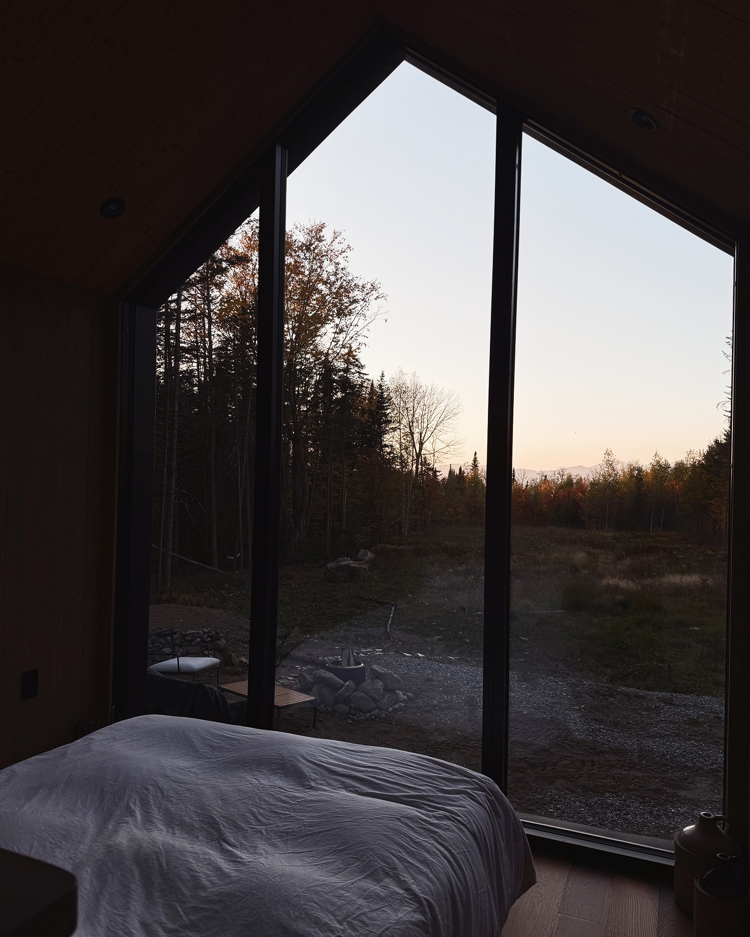 Bed beside a full-height window onto the fire pit at dusk